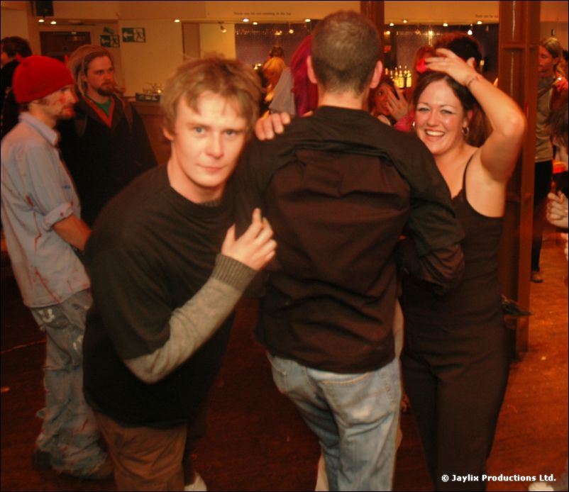 Dancers in a bar, a man in a black top facing the camera and a woman laughing behind him