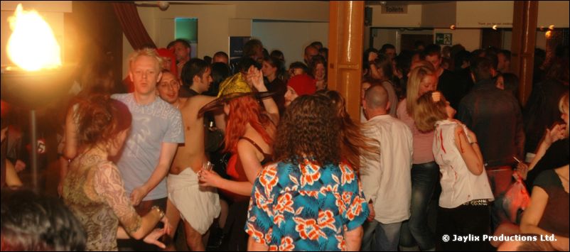 A crowd dancing in a bar, one woman in a floral top with her back to the camera