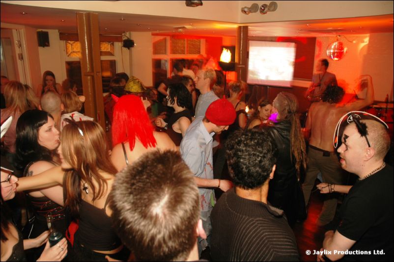 A crowded bar with costumed people dancing, some in hats and wigs