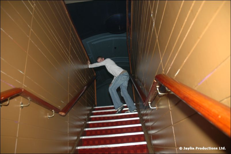 A person leans against the wall on a red-carpeted staircase, seen from below