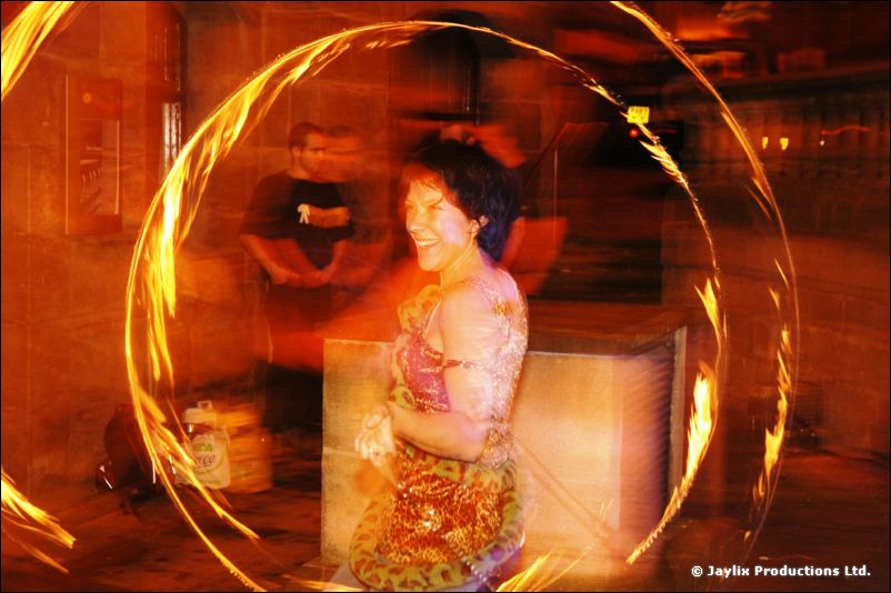 A smiling person in a colourful top stands inside a large blurred ring of fire