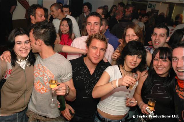 A group of smiling people crowd together for the camera, several holding drinks