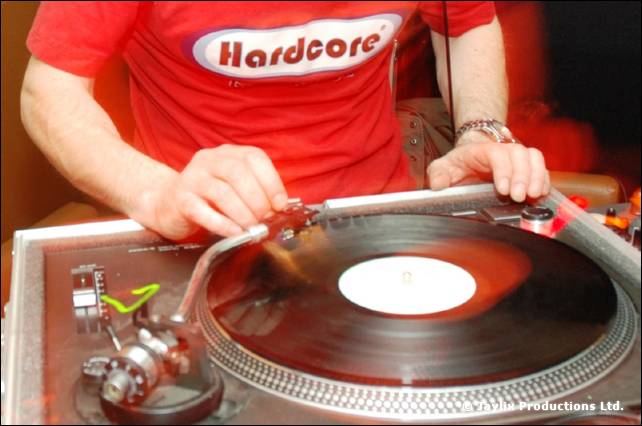A DJ in a red Hardcore t-shirt spins a record on a turntable