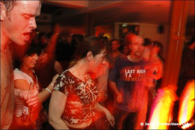 People dance in a bar, one wearing a Last Night a DJ Saved My Life t-shirt, lit in orange