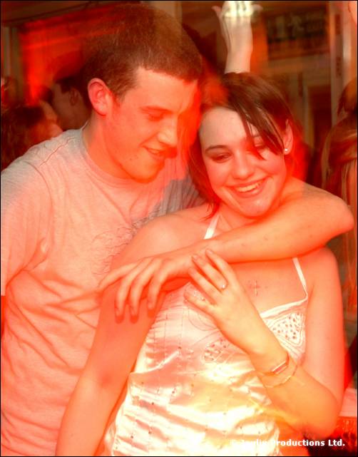 A smiling couple embrace and dance close together in orange light