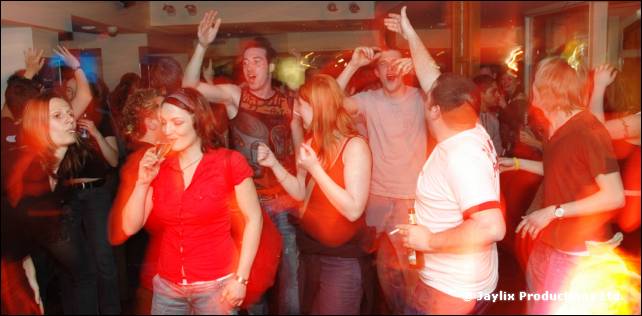 A crowd of people dancing in a bar, a person in a red top at the centre
