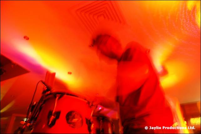 A blurred figure behind a conga drum in a room lit in intense red and yellow