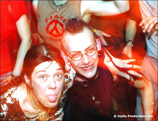 Two people in a crowd pulling faces, one with a pierced face and red mohican, one sticking out their tongue