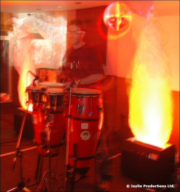 A person sits behind congas with two flame effects lit on either side