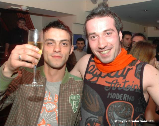 Two people smile for the camera, one holding up a glass of champagne, the other in an orange scarf