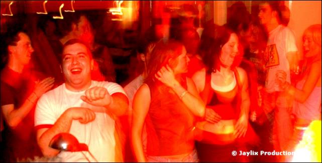 A smiling person in a white t-shirt dancing among others in red light, heavily blurred