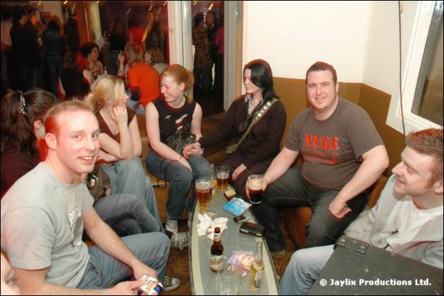 A group sit and smile around a low table with drinks in a corner booth