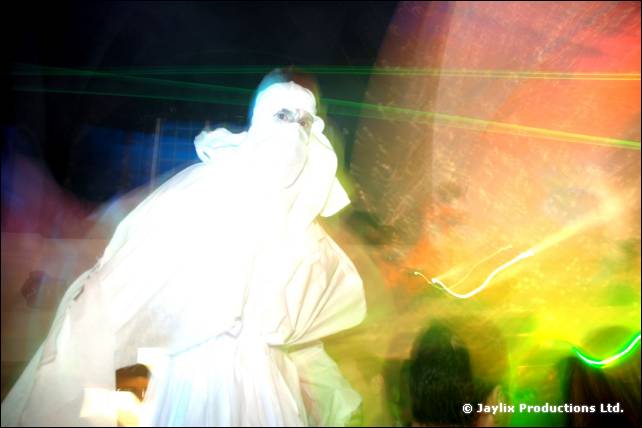 A person in flowing white robes moves through green laser light, blurred