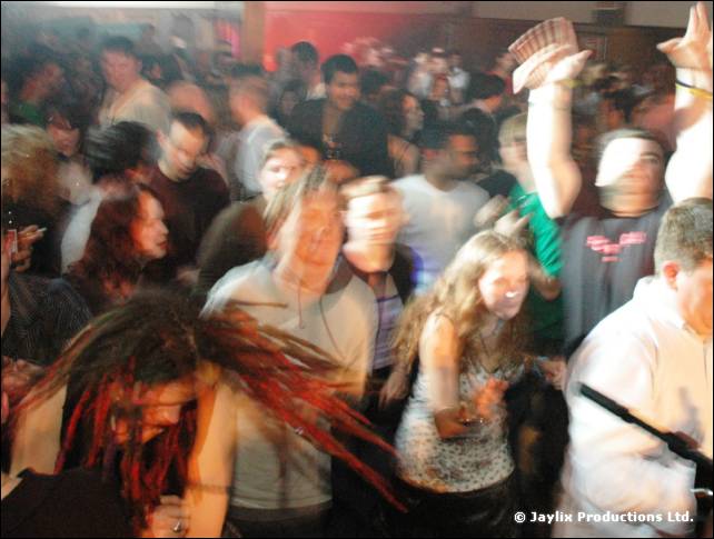 Blurred crowd dancing in a busy club, with a person with long red dreadlocks in the foreground