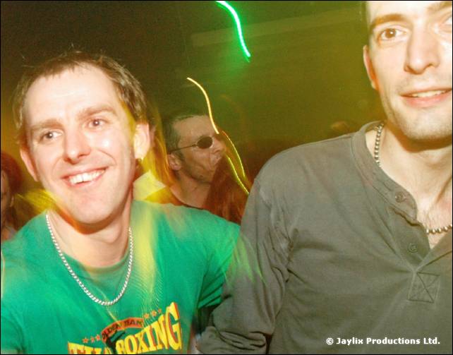 Two smiling men, one in a green Thai Boxing T-shirt, with green light trails behind