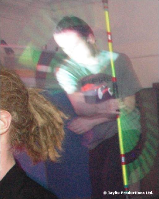 Blurred person in a dark top holds a glowing striped staff, with another person's head in the foreground