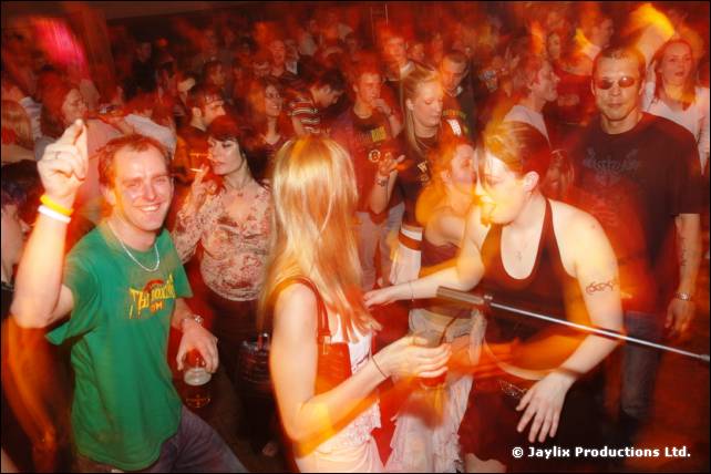 Crowd dancing in a busy hall, with a smiling man in a green T-shirt and a woman with a fire staff