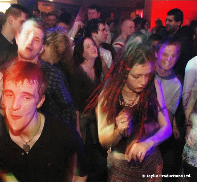Close view of dancers in a crowd, including a woman with dark dreadlocks and a man with red hair in black
