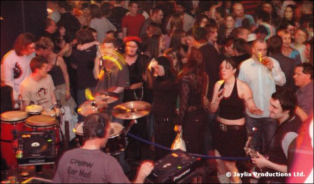 Crowd around a drum kit and DJ in a Crew Bar Med T-shirt, with a rope barrier in front