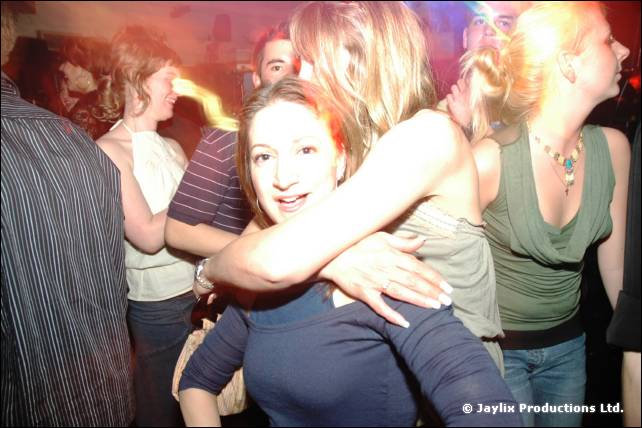 Woman looks at the camera as people dance closely around her in a dim crowd