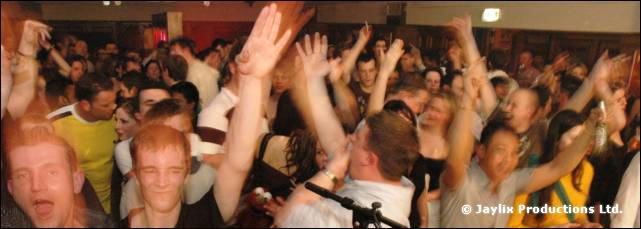 Crowd with raised arms in a hall, with two men shouting in the foreground