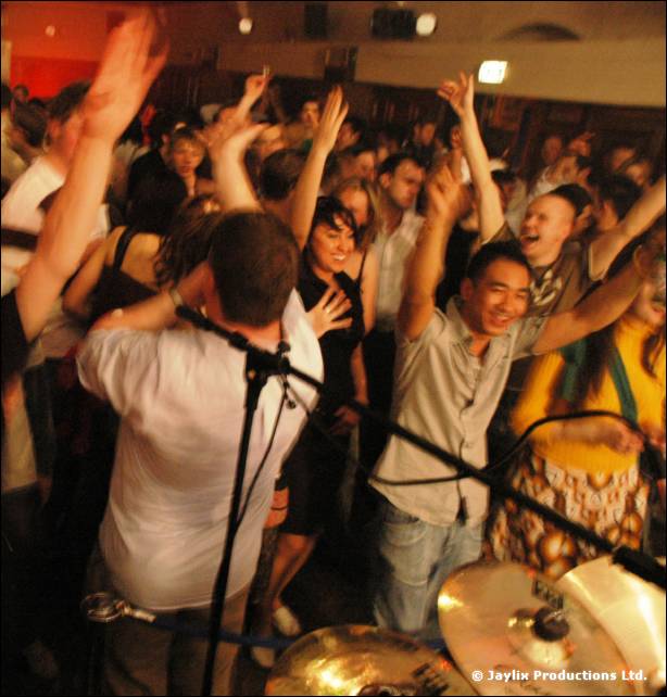 Crowd with raised arms dancing behind a microphone stand and cymbals