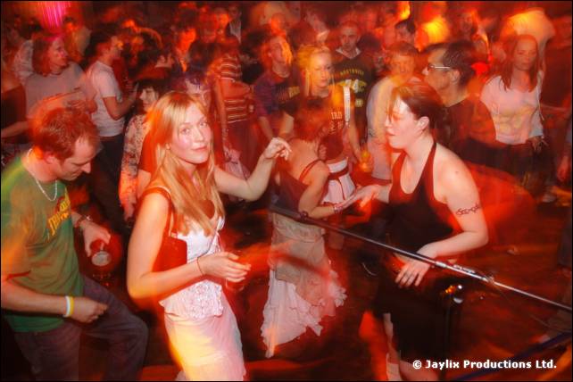 Crowd dancing in a busy hall, with a man in a green T-shirt and a woman in white in the foreground
