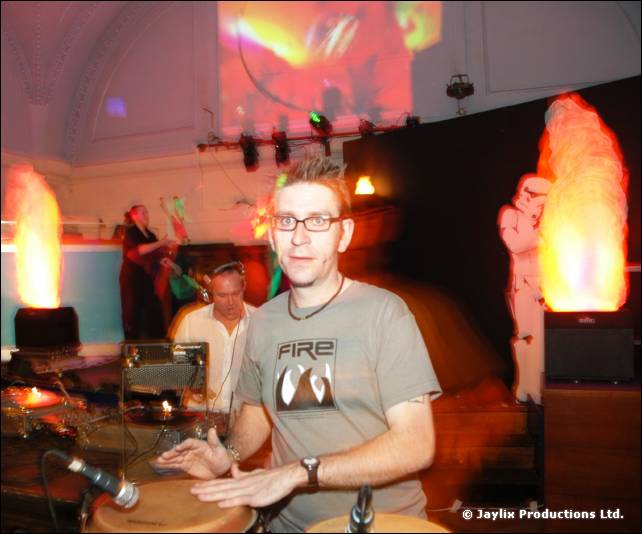 Man in glasses and a grey FIRE T-shirt plays congas, with flame effects and a Stormtrooper cutout behind