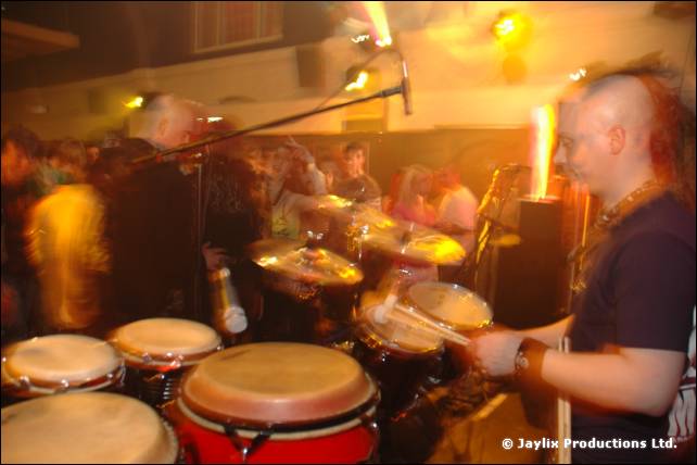 Drummer with a mohican plays a set of drums on stage in a warm lit hall