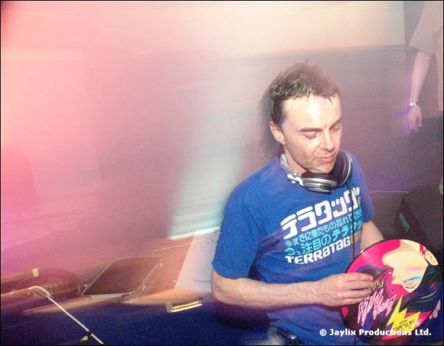 DJ in a blue T-shirt with Japanese print and headphones holds a pink and yellow record