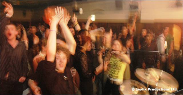 Crowd with raised arms dancing next to a drum kit, in warm blurred light