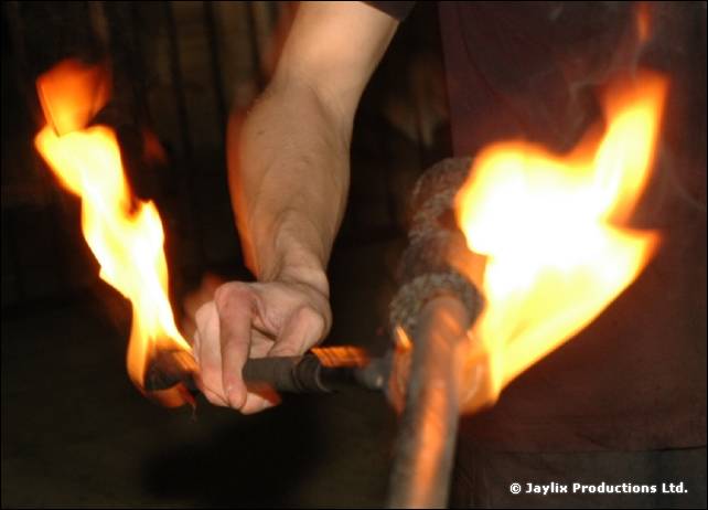 Close view of a hand holding a burning staff, with flames at both ends