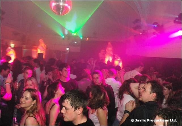 Crowd in a hall lit with pink and green lights, under a mirror ball
