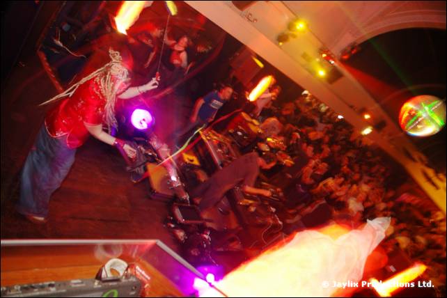 View down from a stage on a person with dreadlocks using equipment, with a crowd beyond and a mirror ball