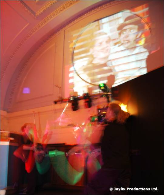 Video screen above the dance floor shows two faces, with a person on a stage below