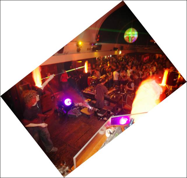 Tilted view of a crowded hall from a stage, with a person on the left and a mirror ball above