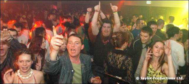 Crowd with raised arms and pointing fingers, in a hall with yellow lighting