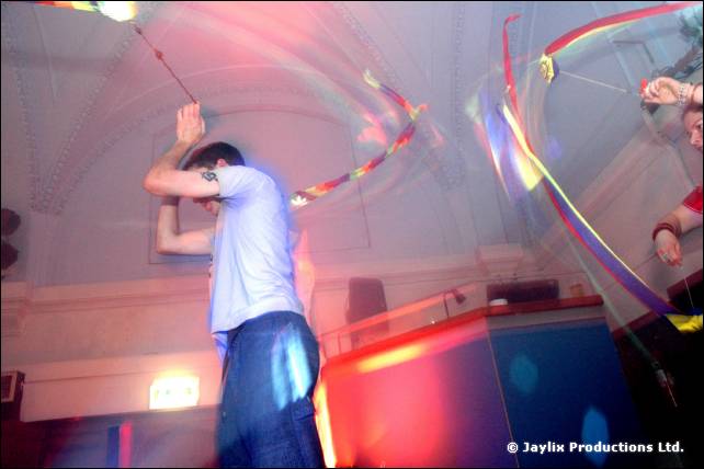 Person in a pale top twirls ribbons of light in front of a DJ booth