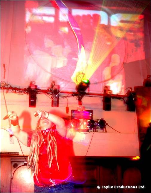 Person with long dreadlocks tips their head back drinking from a bottle, with stage lights and a projection behind