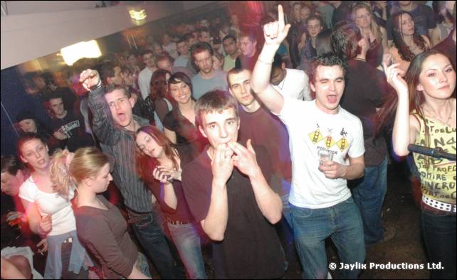 Crowd with raised arms and pointing fingers, including a man in a white T-shirt at the front