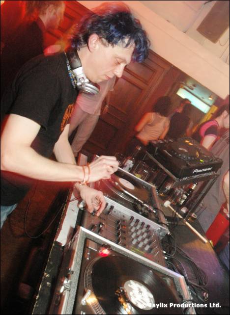 DJ with dark curly hair and headphones mixes at turntables and a Pioneer mixer