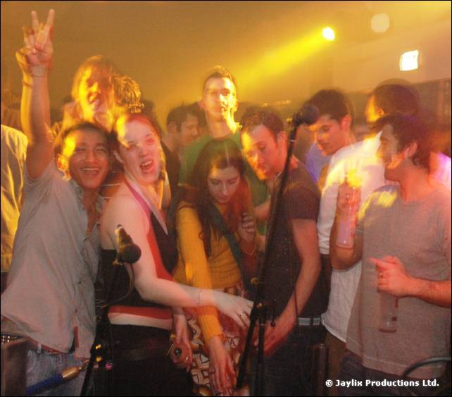 Smiling crowd in yellow light, with a person making a peace sign at the back