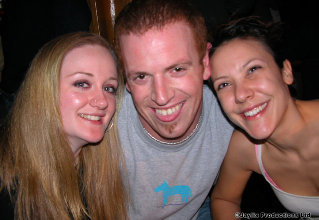 Three people pose cheek to cheek and smile at the camera in a dark room