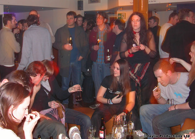 People sit and stand drinking in a crowded lounge area of a bar