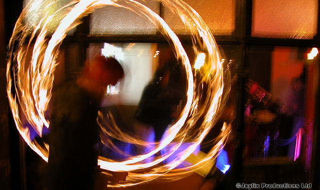 Circles of fire from spinning poi, with a dark blurred figure behind