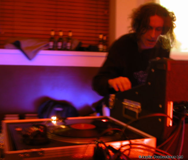 A person with curly hair works at a mixer behind a turntable