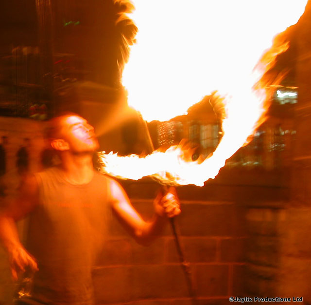 A person breathes a large plume of fire from a torch against a brick wall