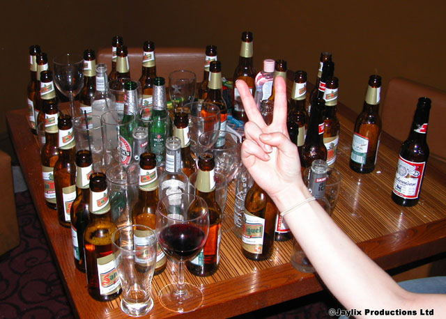 A table crowded with empty bottles and glasses, with a raised hand making a peace sign