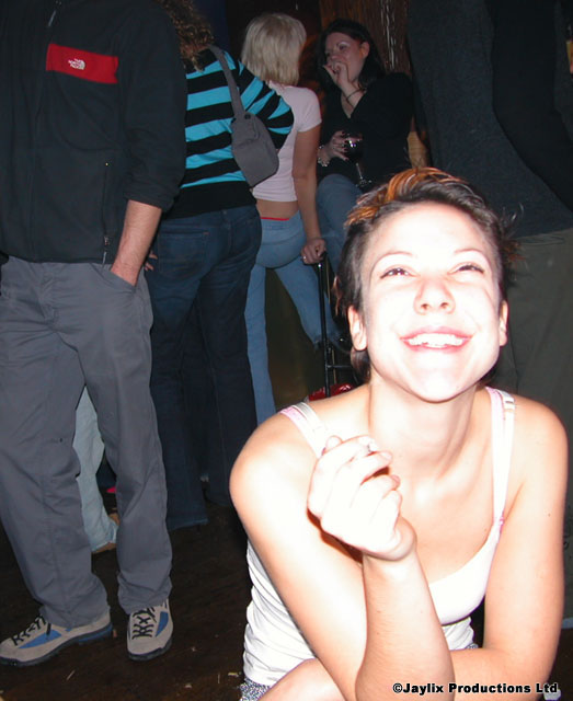 A smiling person with short hair rests their chin on a hand in front of people standing behind