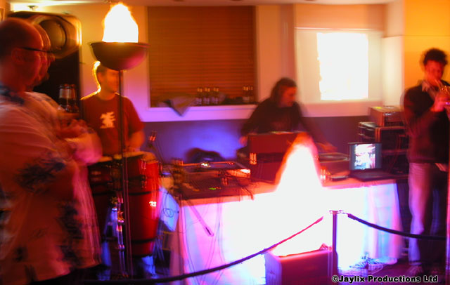 A band and DJ at a lit stage with two flaming torches and a rope barrier in front